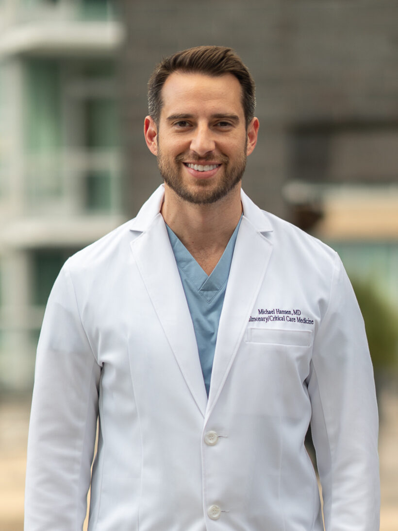 Mike Hansen, MD, in a white coat over scrubs